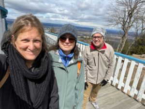 three smiling adults on the top of a mountain on a cold day in March