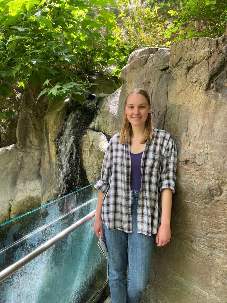 A young woman with straight blond hair standing by a waterfall